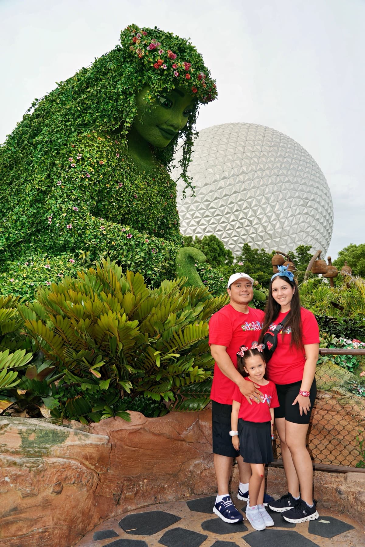 The Garcia family in matching red shirts by the Moana topiary and Spaceship Earth at EPCOT